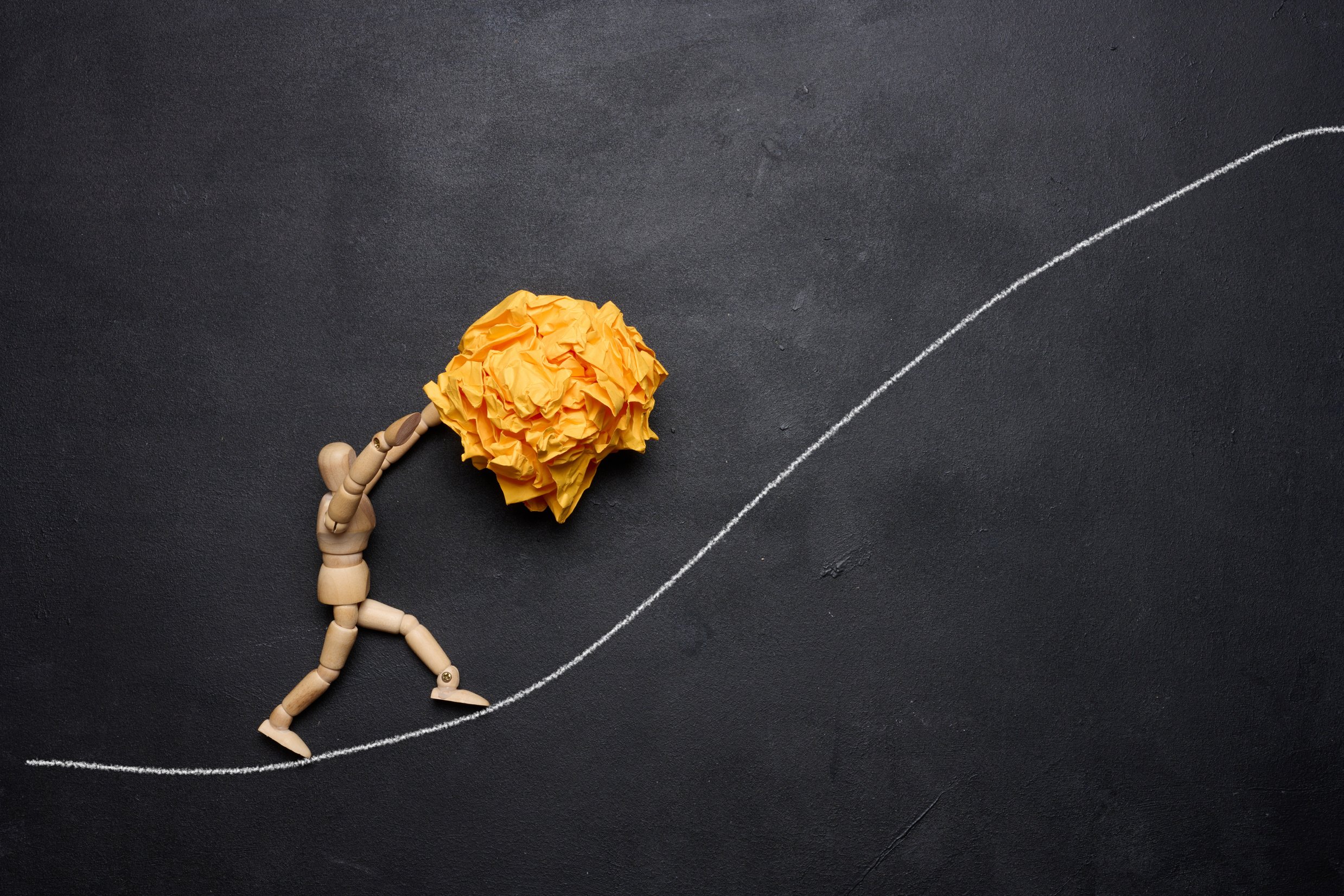 A wooden figurine of a person rolling a crumpled paper ball upwa